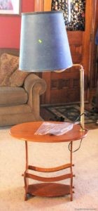 scuffed up wooden end table and attatched lamp with blue broken shade